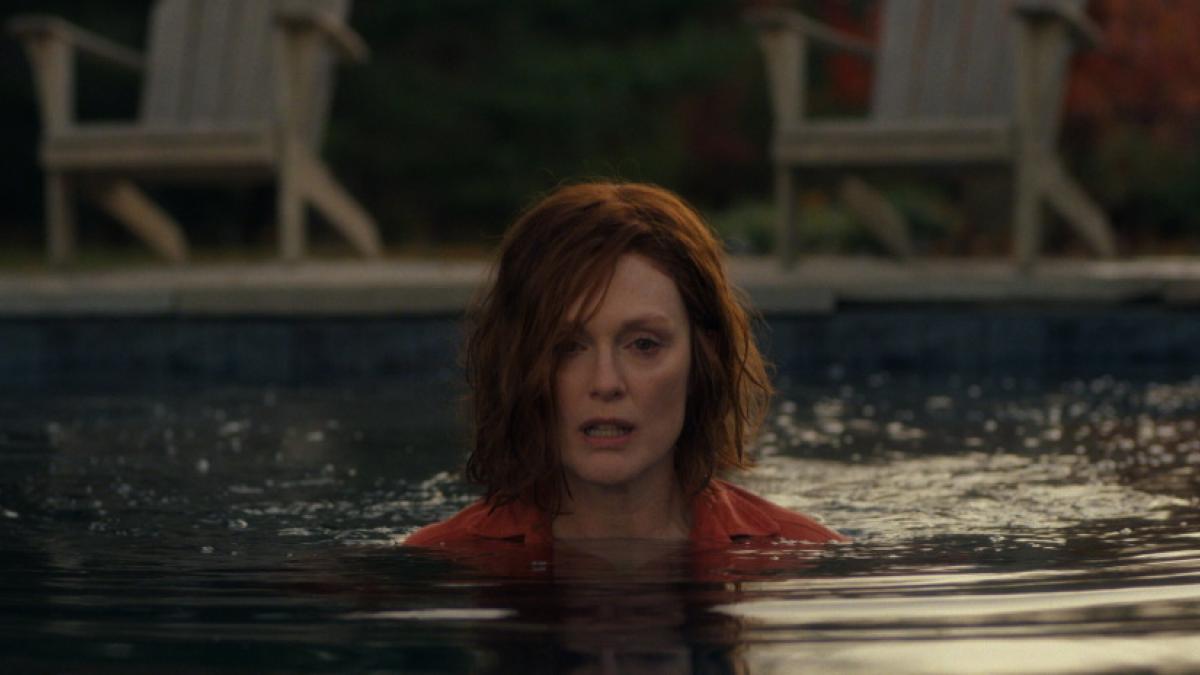 A medium-close shot of a red-haired, middle-aged woman wading in a swimming pool up to her neck.