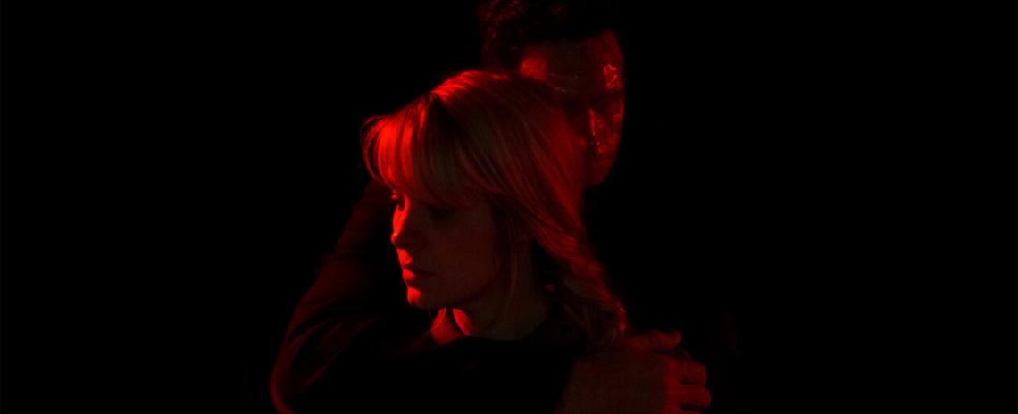 Red-and-black image of a blonde woman being held around the throat by a masked stranger.
